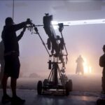 Técnico ajusta equipamento de câmera em estúdio de filmagem envolto em névoa